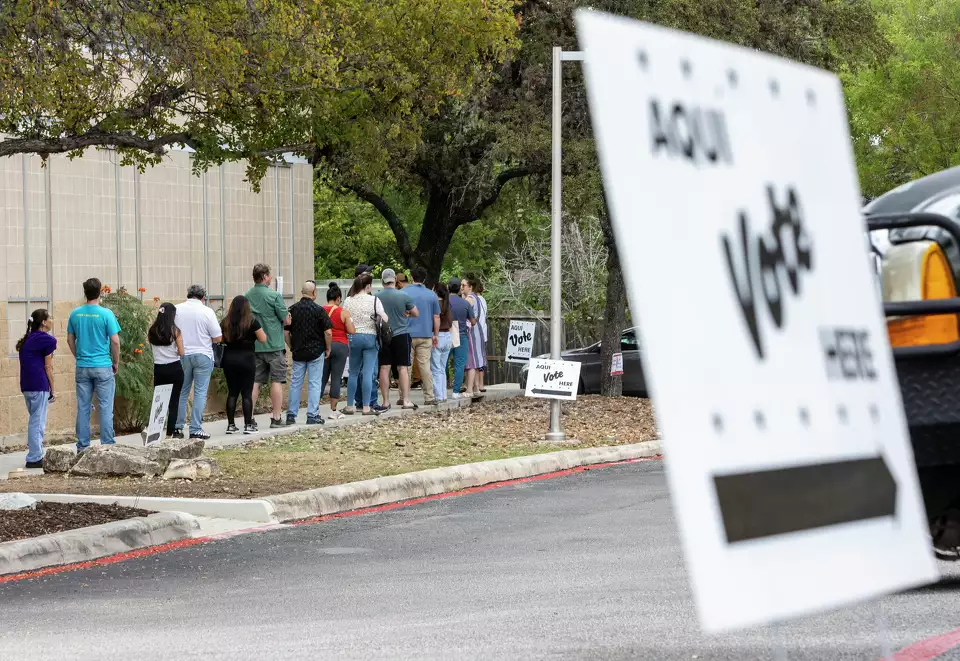 Vote here sign with a line of people outside.